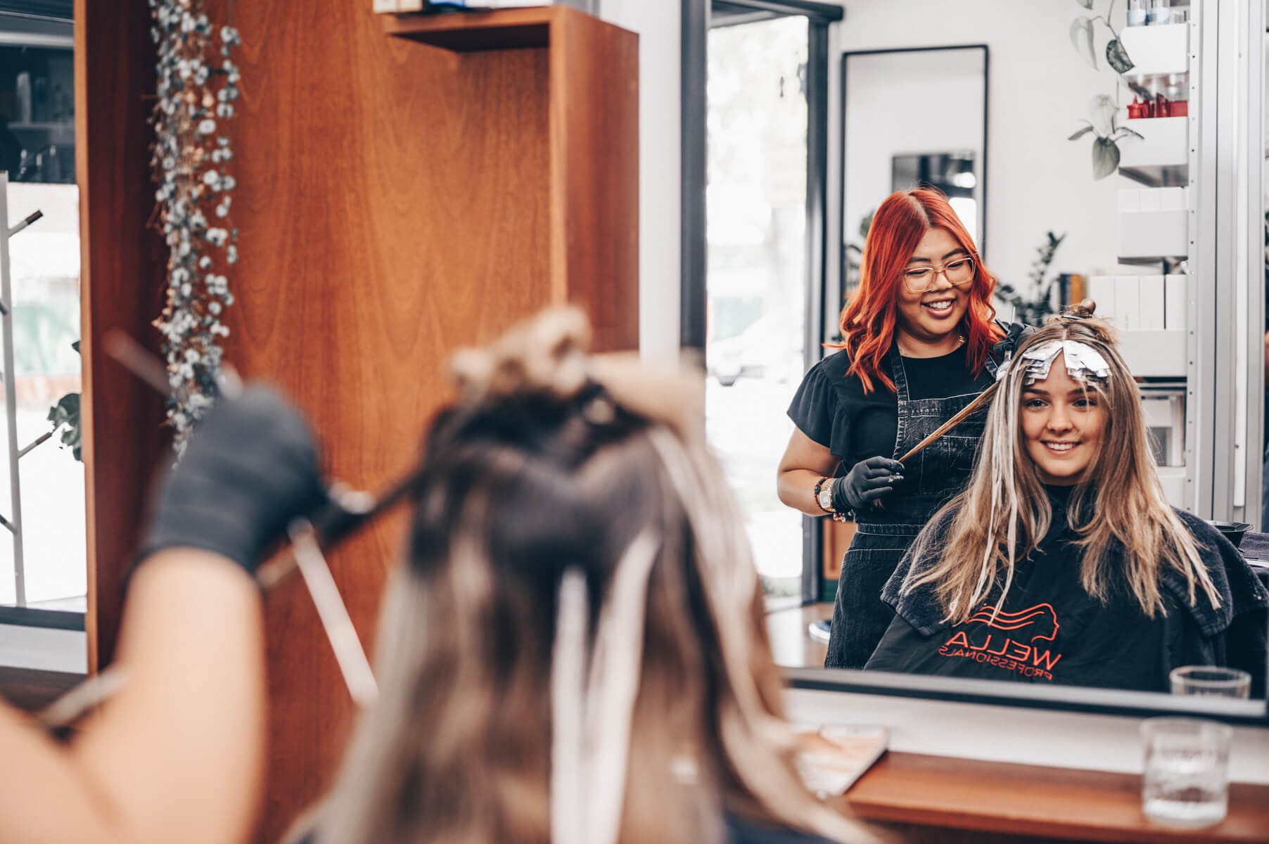 A stylist and client smiling in the mirror during a colour appointment at Juicy Golden